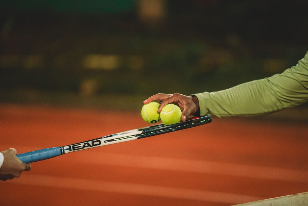 Two people exchanging tennis balls on a clay court during nighttime, focusing on the sport's dynamics.